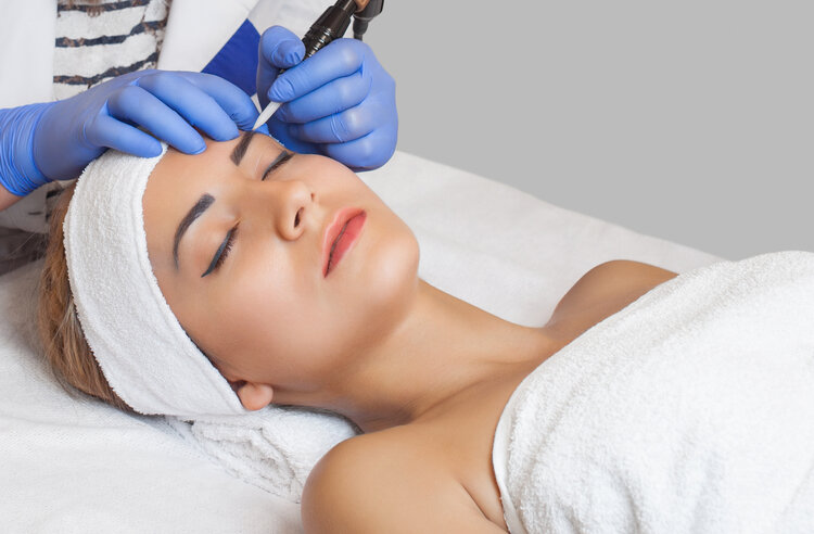 Permanent make-up for eyebrows of beautiful woman with thick brows in beauty salon. Closeup beautician doing tattooing eyebrow. Makeup and Cosmetology concept. | Passion Beauty Academy