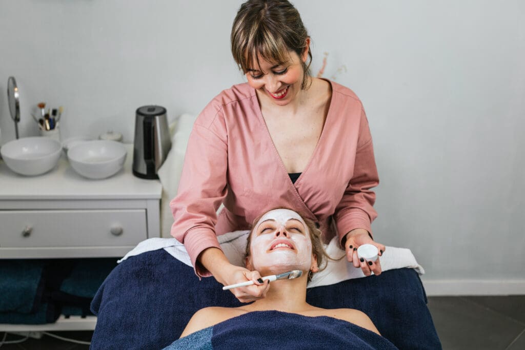 A skincare therapist performing a facial treatment on a client using natural products and tools designed for relaxation and skin health